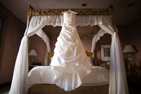 White ballgown hanging from a white and bronze canopy bed - wedding photo by Melissa Jill Photography
